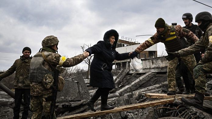 A woman is assisted by Ukrainian servicemen while people cross a destroyed bridge as they evacuate the city of Irpin, northwest of Kyiv, on 5 March 2022 | Photographer: Aris Messinis/AFP/Getty Images via Bloomberg