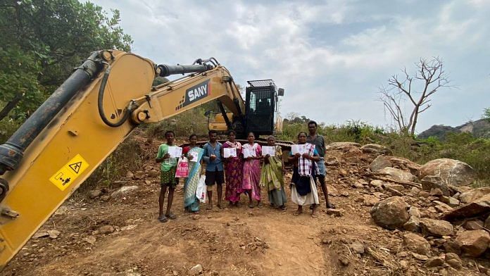 Tribal cashew farmers, with their D-Pattas, stand next to a bulldozer used by the private mining company on Vuralova Hill | Photo: Rishika Sadam