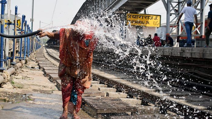 A woman pours water on her face from a pipe on a hot summer day, at the Prayagraj railway station