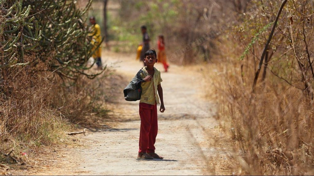 A tribal kid carrying bag looks at passerby as he walks towards his home | Photo: Manisha Mondal | ThePrint