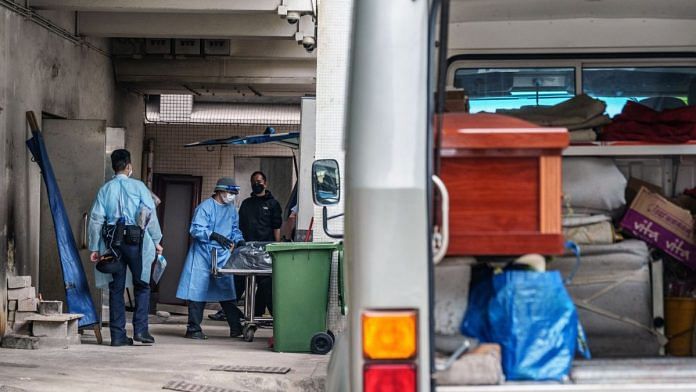 Healthcare workers wearing PPE transport the body of a deceased Covid patient onto a hearse outside the mortuary at the Queen Elizabeth Hospital in Hong Kong | Bloomberg