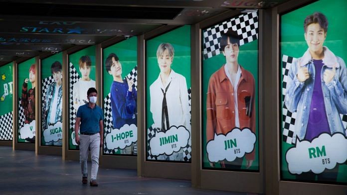 A pedestrian wearing a protective mask walks past an advertisement for K-pop boy band BTS displayed in Seoul, South Korea | Bloomberg