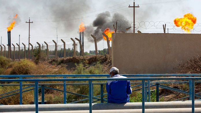 A man sits across flare stacks burning off excess gas at the Nahr Bin Omar oilfield in Iraq's southern province of Basra | Photographer: Hussein Faleh/AFP/Getty Images via Bloomberg