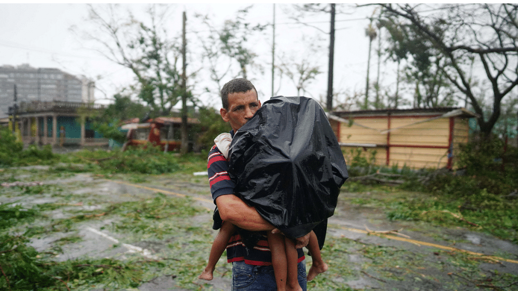 File Photo- A man carries his children next to debris caused by the Hurricane Ian after it passed in Pinar del Rio, Cuba, 27 September, 2022. Reuters/Alexandre Meneghini