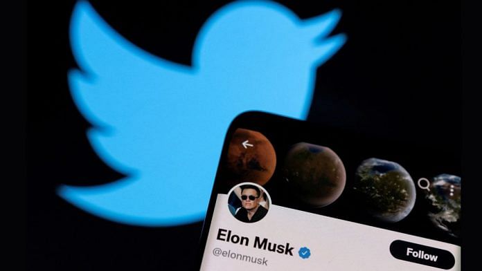 Elon Musk's Twitter account is seen on a smartphone in front of the Twitter logo | Illustration by Dado Ruvic/Reuters