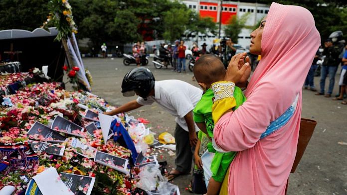 A woman carrying her child prays on a monument as she pays condolence to the victims after a riot and stampede following soccer match between Arema vs Persebaya, outside the Kanjuruhan stadium in Malang, East Java province, Indonesia, 3 October 3, 2022 | Reuters