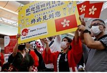 File Photo of members from Japan's shopping and tourism companies hold a placard reading 'Welcome back to Japan! We finally met you!' as they greet a group of tourists from Hong Kong upon their arrival at Haneda airport. 26 June, 2022 | Reuters