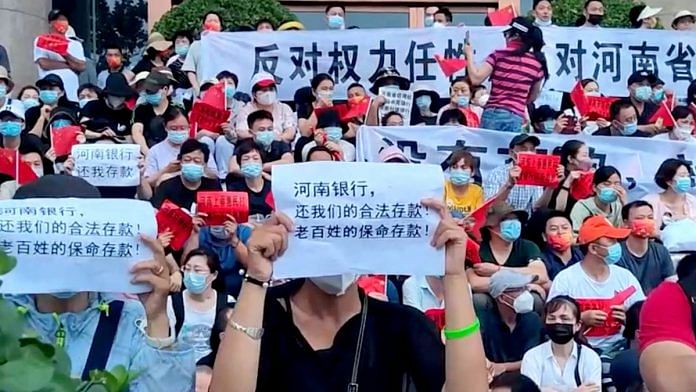 File Photo of demonstrators hold up signs during a protest over the freezing of deposits by some rural-based banks, in Zhengzhou ,China July 10, 2022 | Reuters