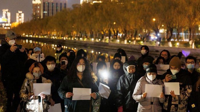 People gather for a vigil and hold white sheets of paper in protest over coronavirus disease (COVID-19) restrictions, during a commemoration of the victims of a fire in Urumqi, as outbreaks of COVID-19 continue, in Beijing, China | Thomas Peter, Reuters