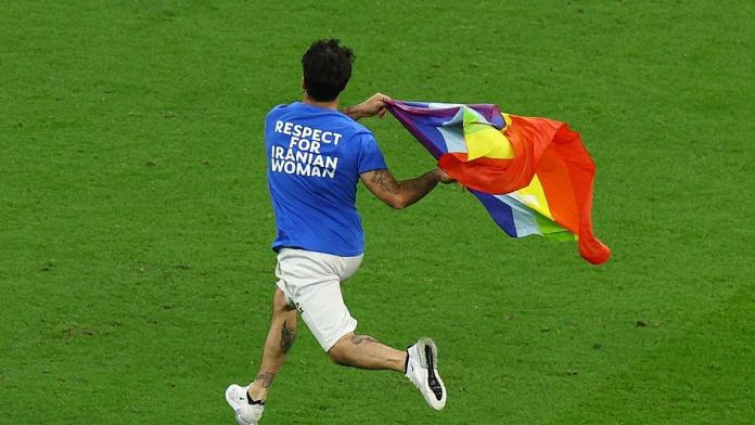 A pitch invader runs onto the field wearing a t-shirt with a message saying 'Respect for Iranian Women' and holding a rainbow flag during the match at Lusail Stadium, Qatar on 28 November, 2022 | Reuters
