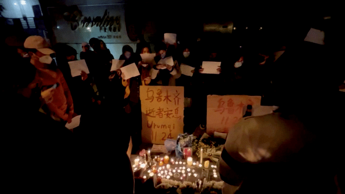 People hold signs and light candles during a vigil held for the victims of the Urumqi fire, in Shanghai | Gao Ming/via Reuters