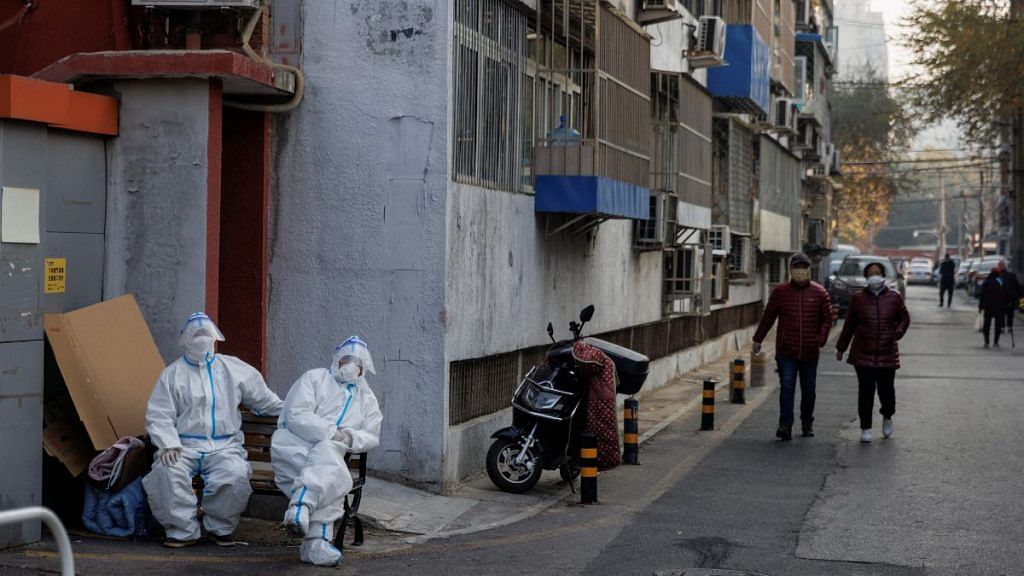 Epidemic prevention workers in protective suits sit in a locked-down residential compound as the Covid outbreaks continue in Beijing, on 23 November 2022 | Reuters/Thomas Peter
