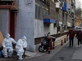Epidemic prevention workers in protective suits sit in a locked-down residential compound as the Covid outbreaks continue in Beijing, on 23 November 2022 | Reuters/Thomas Peter