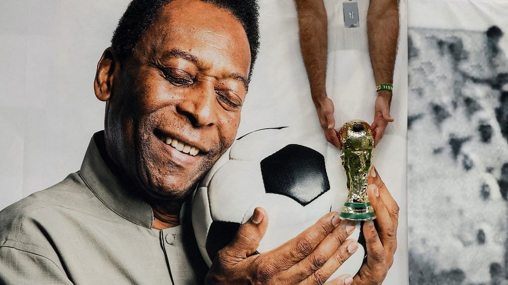 A Brazil fan holds a replica World Cup trophy in front of a banner of former Brazil player Pele | File Photo: Reuters/Benoit Tessier