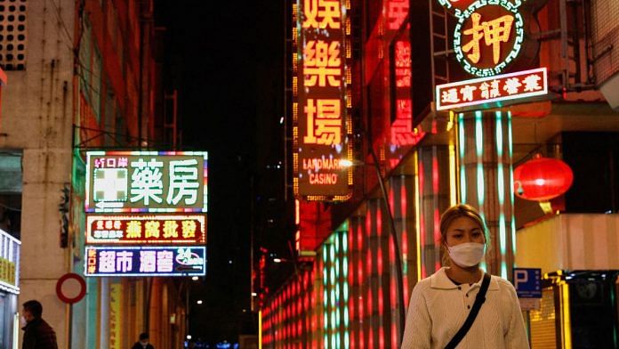 File photo of a woman wearing face mask walking under neon lights during the Covid-19 pandemic in Macau, China, on 29 December, 2022 | Reuters