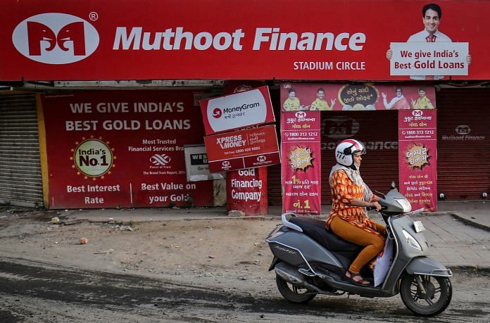 Representational photo of a woman riding her scooter past a Muthoot Finance branch | Reuters