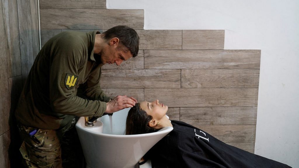 Hairdresser and Ukrainian Territorial Defence unit volunteer Oleksandr Shamshur, 41-year-old, washes hair of his client Oleksandra at a beauty salon in Kyiv | Reuters