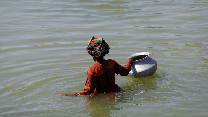 A displaced woman wades through flood water with a water pot, following rains and floods during the monsoon season in Sehwan, Pakistan | Reuters/Akhtar Samroo