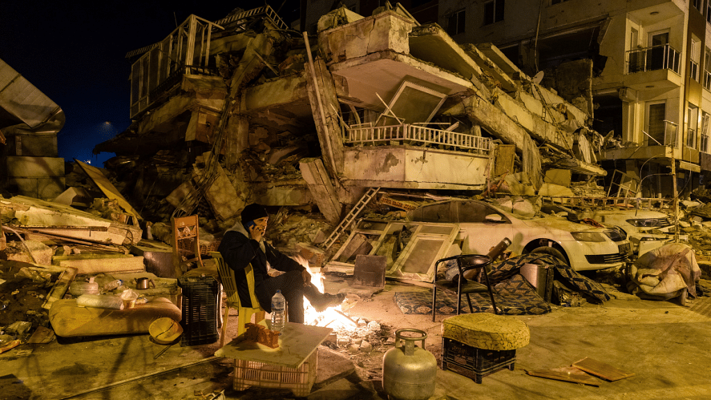 A man speaks on the phone as he sits by a fire near a destroyed building in the aftermath of a deadly earthquake in Antakya, Turkey 20 February, 2023. Reuters/Maxim Shemetov