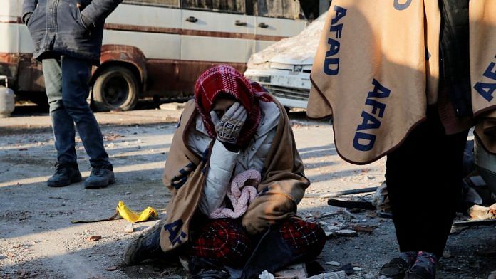 A woman reacts as she sits next to the site of a collapsed building following an earthquake in Kahramanmaras, Turkey, on 8 February 2023 | Reuters/Dilara Senkaya