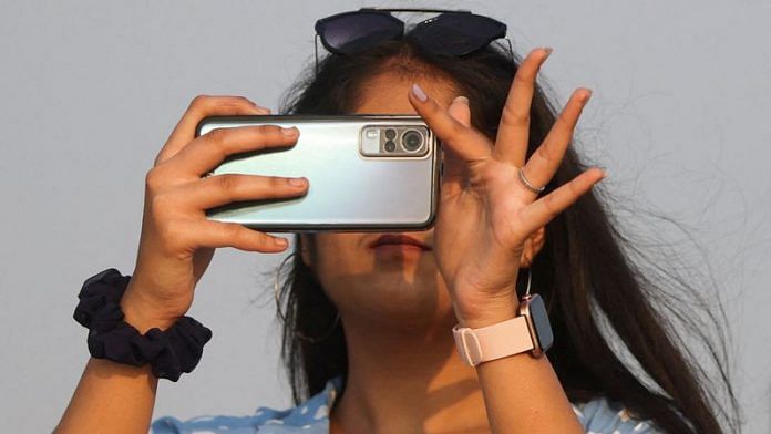 A woman uses a smartphone on a beach in Mumbai | File photo: Reuters