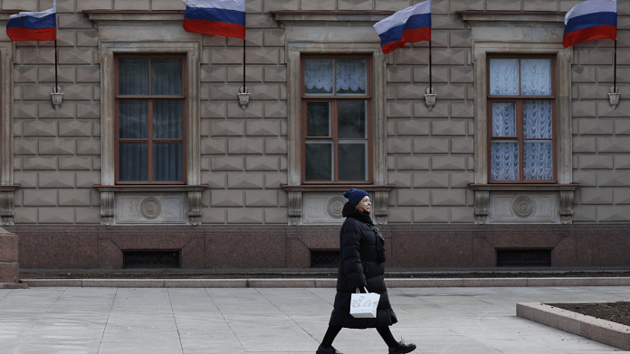 A woman walks past a building with Russian flags placed on its wall in Saint Petersburg, Russia 24 April, 2022 | Reuters/Anton Vaganov