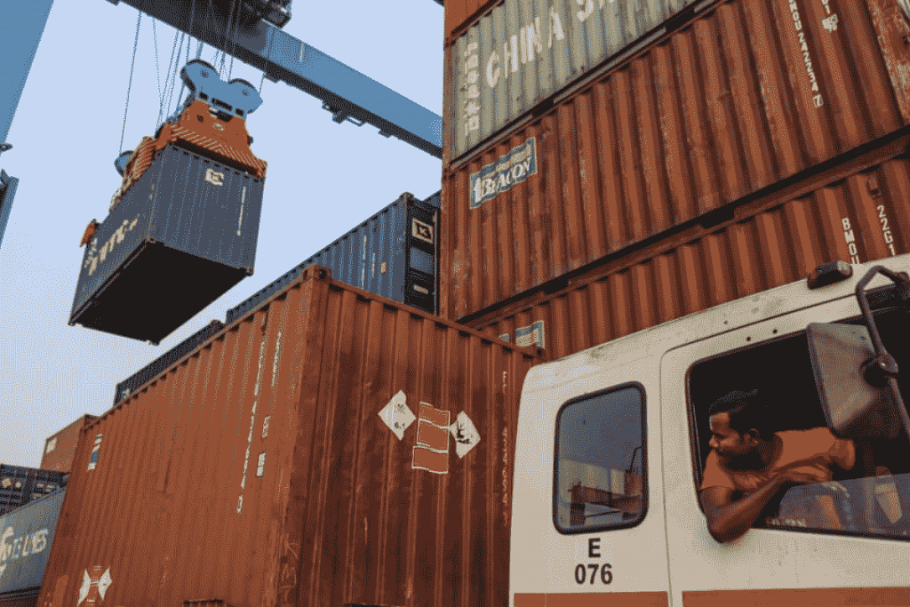 A truck driver watches a reach gantry crane move a shipping container at the Jawaharlal Nehru Port in Navi Mumbai | Representational image | Bloomberg A truck driver watches a reach gantry crane move a shipping container at the Jawaharlal Nehru Port in Navi Mumbai | Representational image | Bloomberg