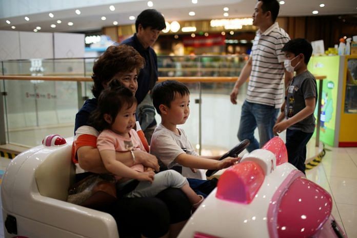 A person holds a girl as a boy drives a toy car at a shopping mall in Shanghai, China on 1 June, 2021 | Reuters