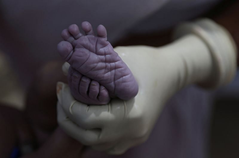 A nurse holds the feet of a newborn baby | Reuters