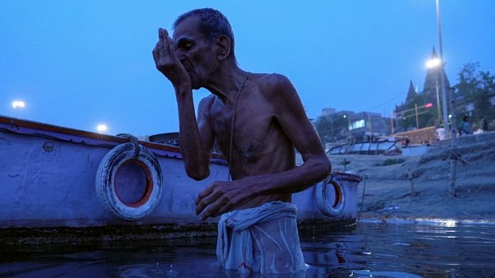 An 82-year-old retiree Murali Mohan Sastry drinks water from the Ganges River during morning prayer in Varanasi | Reuters