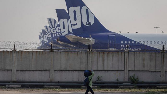 A man carries his bag as he walks past the Go First airline, formerly known as GoAir, passenger aircrafts parked on the tarmac at the airport in New Delhi | Reuters