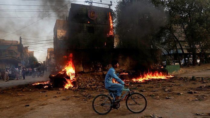 A boy rides past a paramilitary check post, that was set afire by the supporters of Pakistan's former Prime Minister Imran Khan, during a protest against his arrest, in Karachi on 9 May 2023 | Photo: Reuters