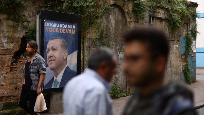 People walk past a sign featuring Turkish President Tayyip Erdogan after he was declared the winner in the second round of the presidential election, in Istanbul, on 29 May 2023 | Reuters/Hannah McKay