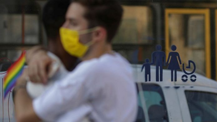 A gay couple hugs during a LGBTQ+ pride parade near a bus stop that has anti-LGBT graffiti message sprayed on it, in Bucharest, Romania | Inquam Photos/Octav Ganea via Reuters