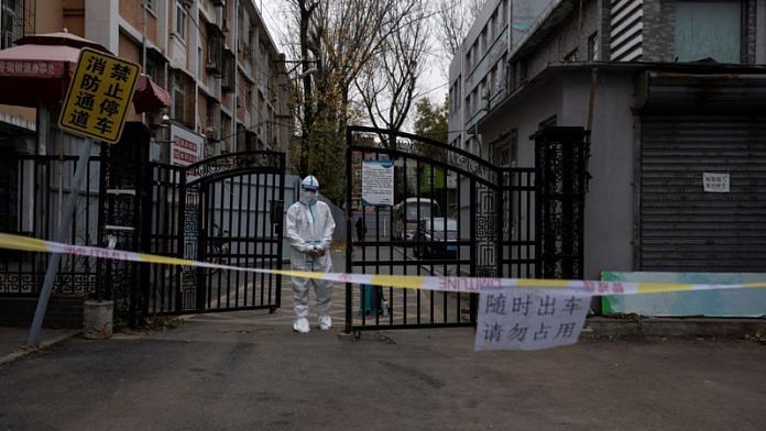 An epidemic-prevention worker in a protective suit stands guard at the gate of a residential compound as coronavirus disease (COVID-19) outbreaks continue in Beijing | File Photo: Reuters