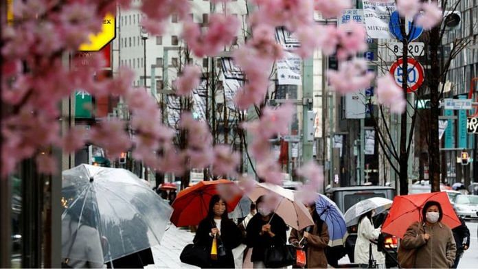 Pedestrians wearing protective face masks are seen behind artificial cherry blossom decorations at a shopping district in Tokyo, Japan | Reuters file photo