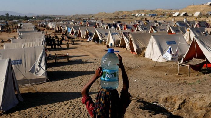 A displaced girl carries a bottle of water she filled from nearby stranded flood-waters, as her family takes refuge in a camp, in Sehwan, Pakistan | Reuters file photo