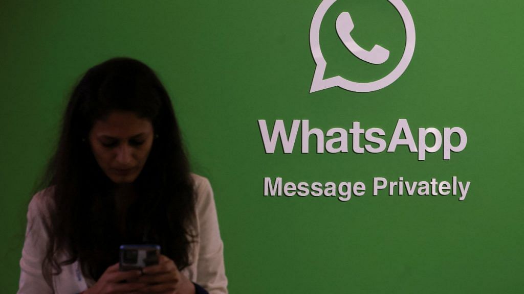 A woman uses her phone next to a logo of the WhatsApp application during Global Fintech Fest in Mumbai | Reuters