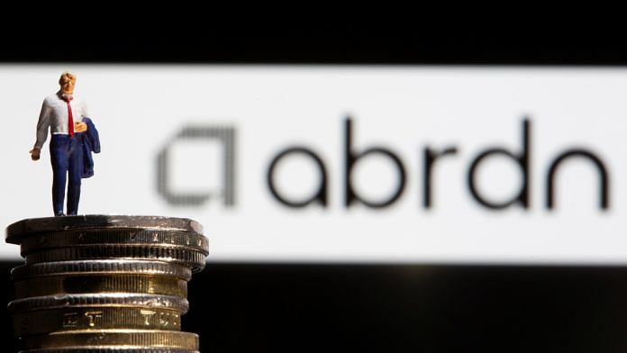 Businessman toy figure is placed on U.K. Pound coins in front of displayed Abrdn logo in this illustration taken | Reuters
