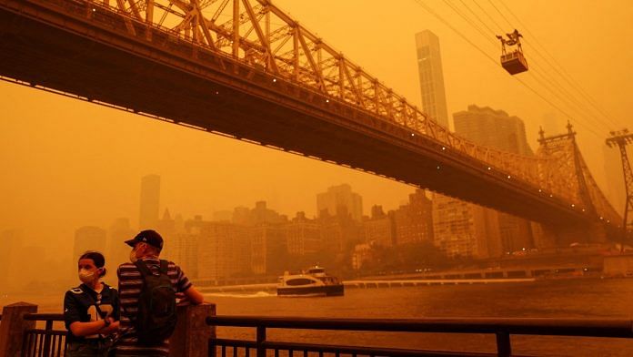 People wear protective masks as the Roosevelt Island Tram crosses the East River while haze and smoke from the Canadian wildfires shroud the Manhattan skyline, June 7, 2023 | Reuters/Shannon Stapleton