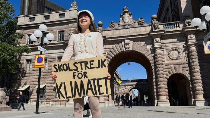 Greta Thunberg stands with a sign that reads, 