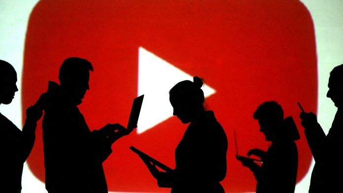 Silhouettes of laptop and mobile device users are seen next to a screen projection of the YouTube logo in this picture illustration taken | Reuters/Dado Ruvic//File Photo