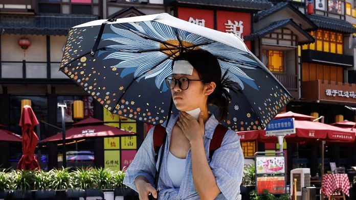 A woman walks with cold patches on her forehead and neck amid a red alert for heatwave in Beijing, China | Reuters/Tingshu Wang