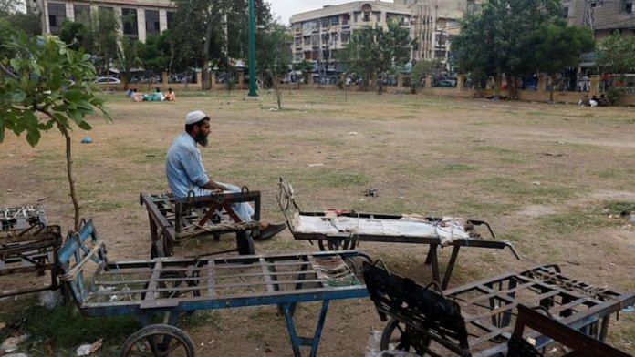 A labourer waits for work while sitting beside push trollies outside a market in Karachi | Reuters/Akhtar Soomro