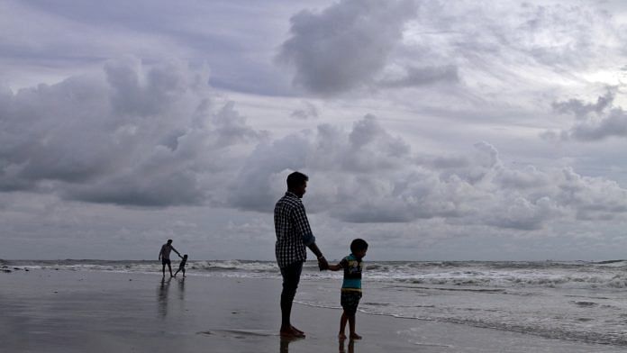 A boy holds his father's hand as they walk on a beach in the backdrop of pre-monsoon clouds in Kochi | Reuters file photo