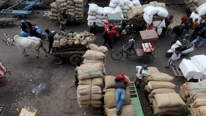 A labourer sleeps on sacks as traffic moves past him in a wholesale market in the old quarters of Delhi | Reuters file photo