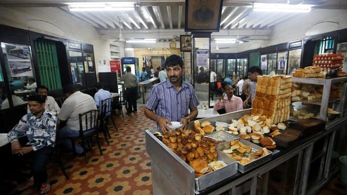 A waiter arranges plates at a counter stacked with breakfast items at an Iranian Parsi restaurant in Mumbai | Reuters