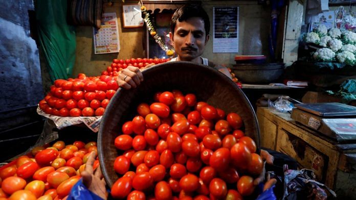 A vendor loads tomatoes in a bag for a customer at a wholesale vegetable market in Mumbai, India | Reuters