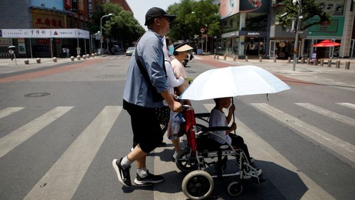 Pedestrians cross a road on a hot day amid an orange alert for heatwave, in Beijing, on 16 July 2023 | Reuters