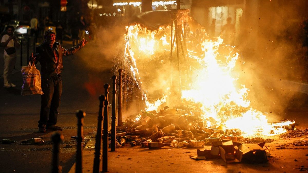 A man gestures next to a burning container as people protest against police violence, in Paris, France | Reuters